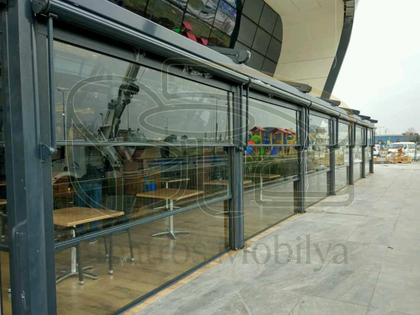 Albatros Mobilya Guillotine-Glasmodell 06; Es erstreckt sich entlang der langen Geschäftsfassade zur Straße hin mit ihren grau getönten Profilen und horizontalen Glasflächen.